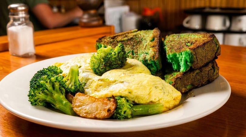 A breakfast plate with fluffy yellow omelets, green broccoli, roasted potatoes, and green French toast.