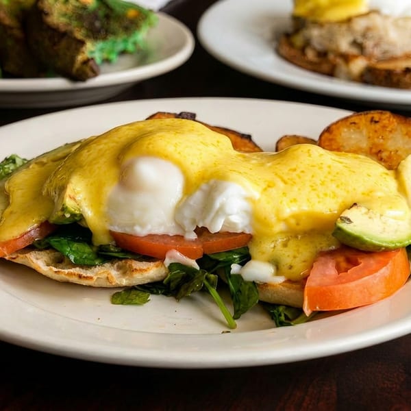 Eggs Benedict with avocado, tomato, and spinach, served with roasted potatoes.