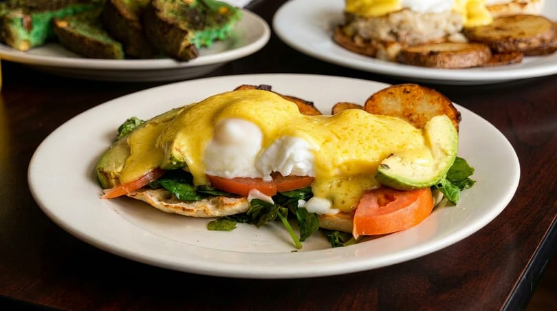 Eggs Benedict with avocado, tomato, and spinach, served with roasted potatoes.