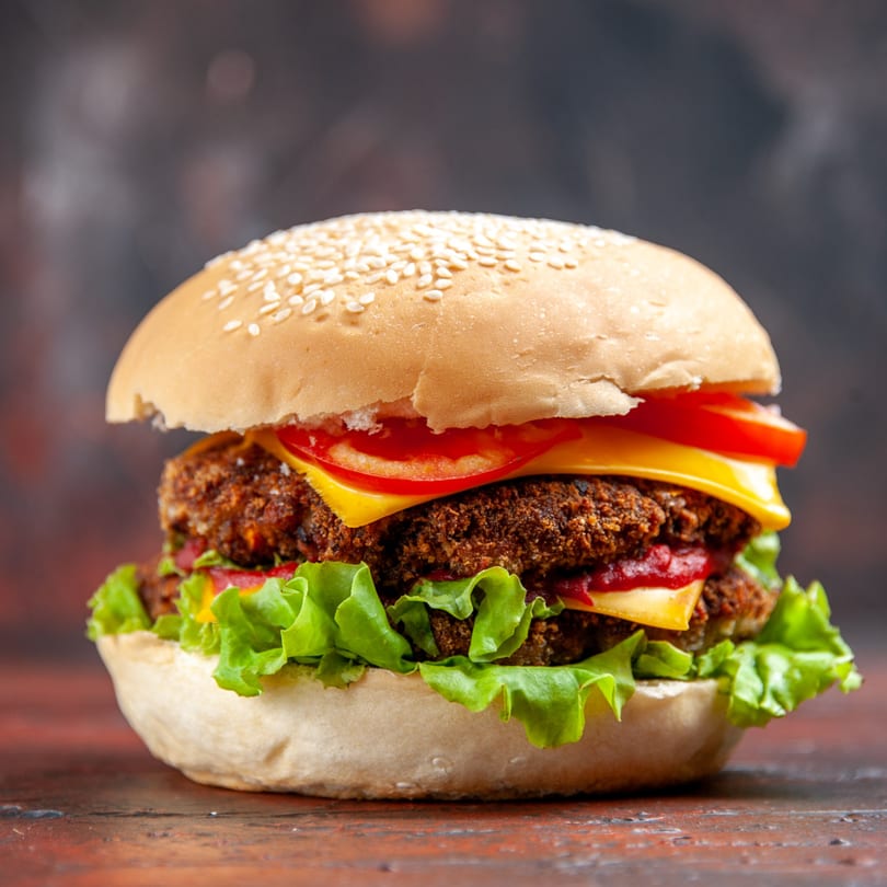 Close-up of a large burger with two patties, cheese, lettuce, and tomato on a sesame seed bun.