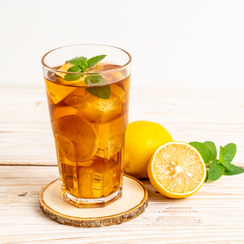 Iced tea with lemon slices and mint leaves in a tall glass on a wooden coaster.